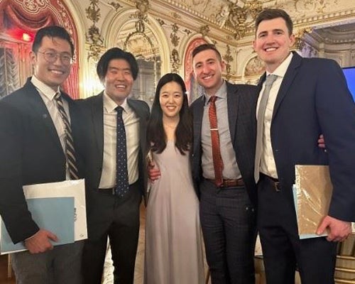 Five students stand together in an ornate room