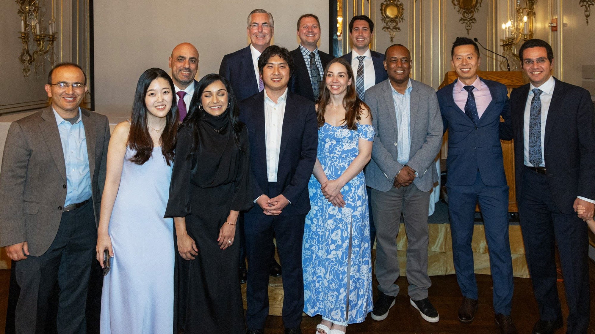 A group of students and faculty stand together in an ornate room